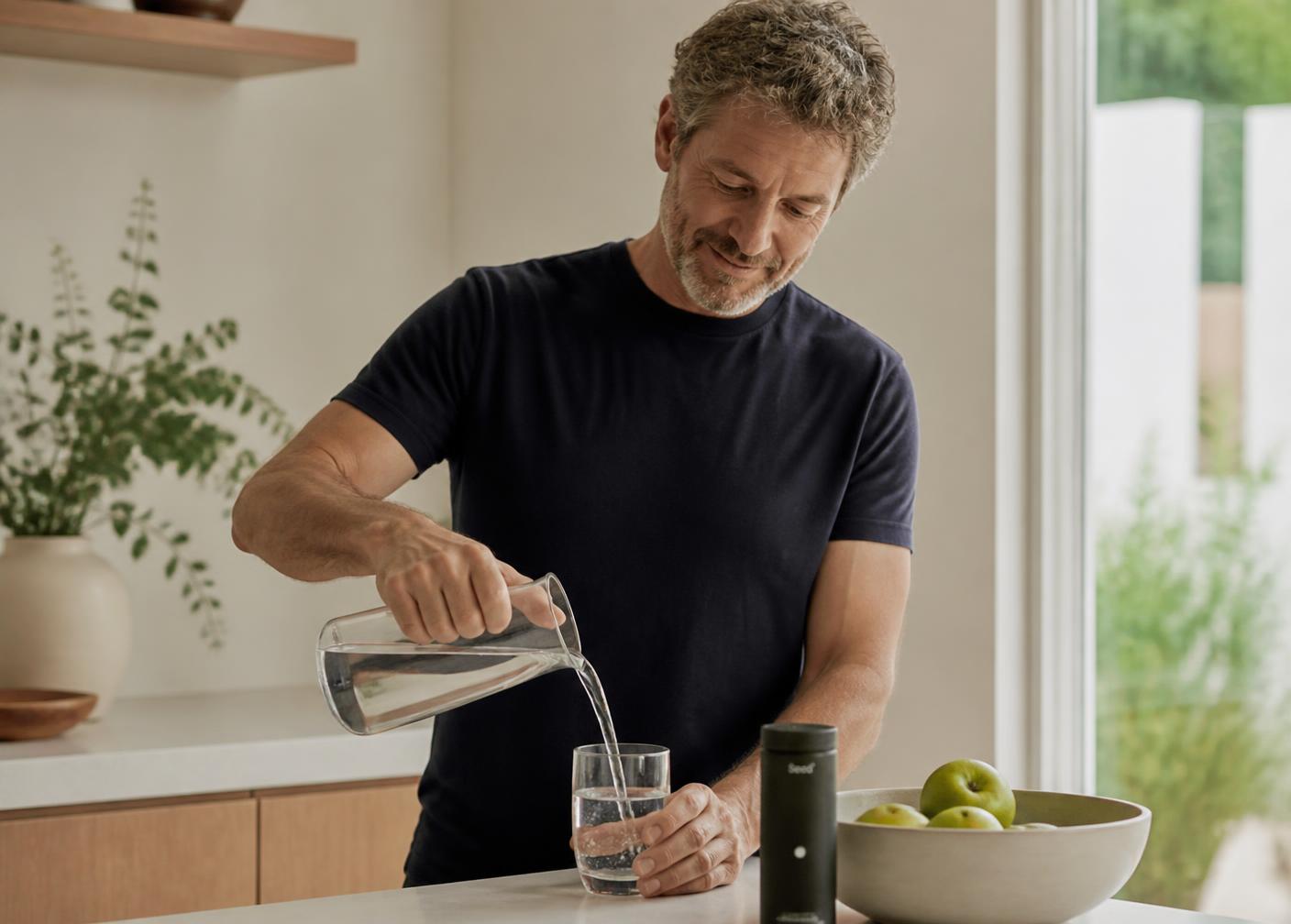 A man in his late forties pouring water in a bright kitchen in the morning